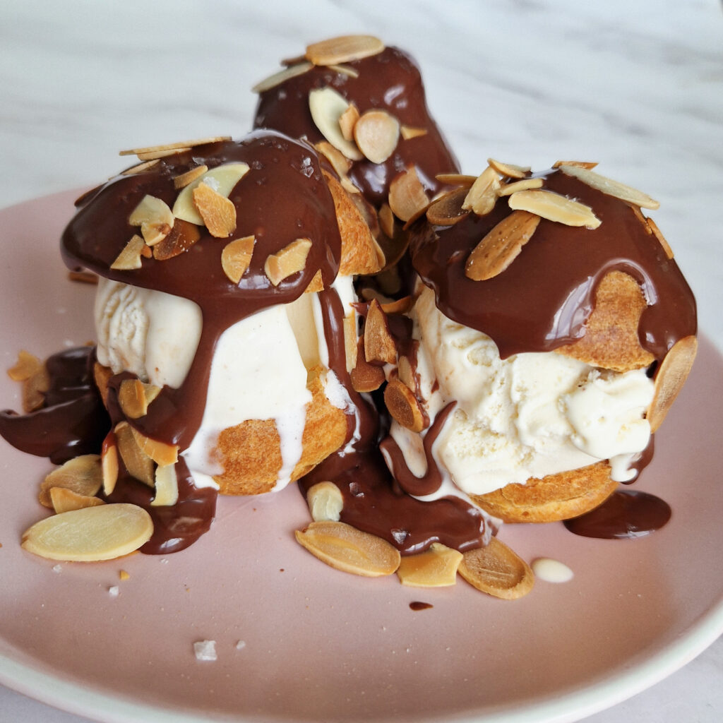 Finished profiteroles with ice cream, chocolate sauce, toasted almonds and flakey salt.